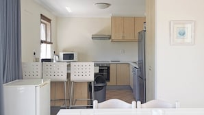 A compact kitchen with a microwave, stove, and refrigerator. There are two chairs at a table with a candle. - Seahorse (Plettenberg Bay)