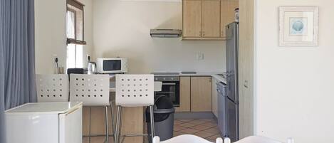 A compact kitchen with a microwave, stove, and refrigerator. There are two chairs at a table with a candle.