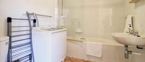 Une salle de bain équipée de toilettes, d’un lave-linge, d’une douche à parois de verre et d’un lavabo.