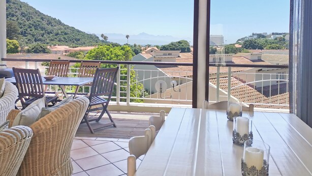A balcony with a table and chairs, overlooking a cityscape with buildings and greenery. - Seahorse (Plettenberg Bay)