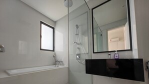 Een moderne badkamer met een douche in een glazen cabine, een witte badkuip en een zwart wastafelmeubel met spiegel.