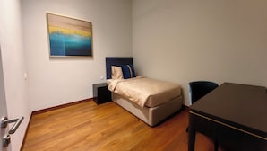 Een kleine, verzorgde slaapkamer met een bed, nachtkastje, stoel en een schilderij aan de muur.