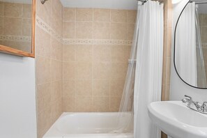 A bathroom with beige tiled walls, a white bathtub, a white sink, and a shower curtain.
