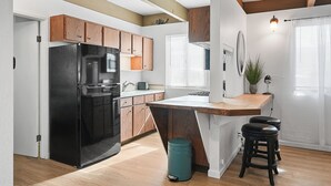 A modern kitchen with wooden cabinets, a black refrigerator, a wooden island with stools, and a teal trash bin. - Mission Bay Condo - Steps to Sand, Dining, AC, Parking, Location & Shops! (San Diego)