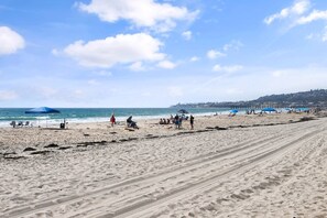 A beach with people, umbrellas, and a pier in the background.