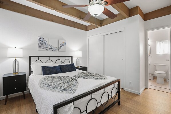 A bedroom with a bed, bedside tables, a ceiling fan, and a door leading to a bathroom.