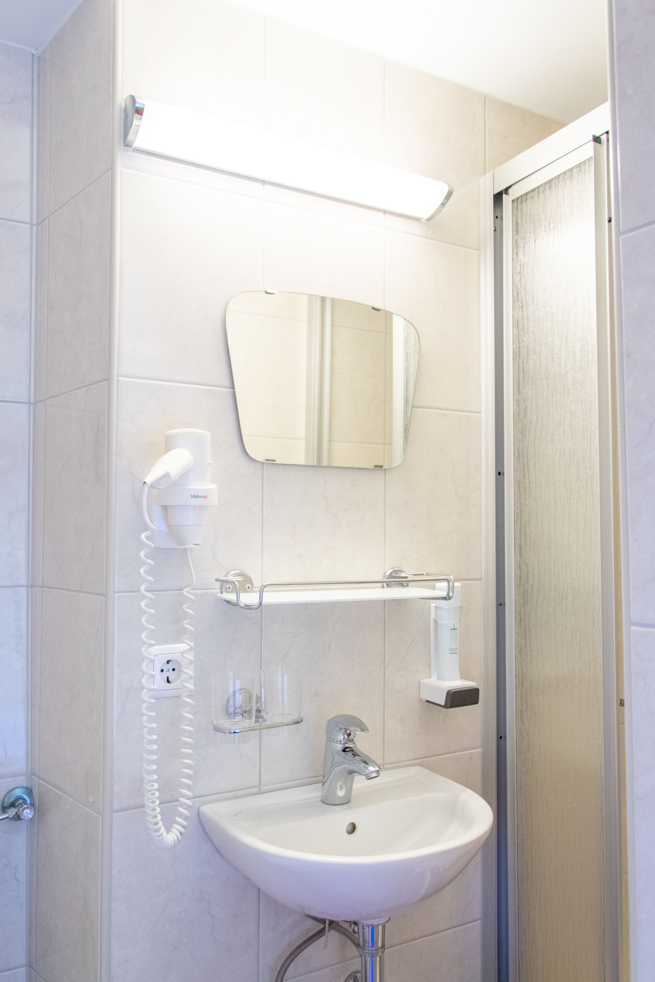 Une salle de bain avec un lavabo blanc, un miroir, un sèche-cheveux et un porte-serviettes.