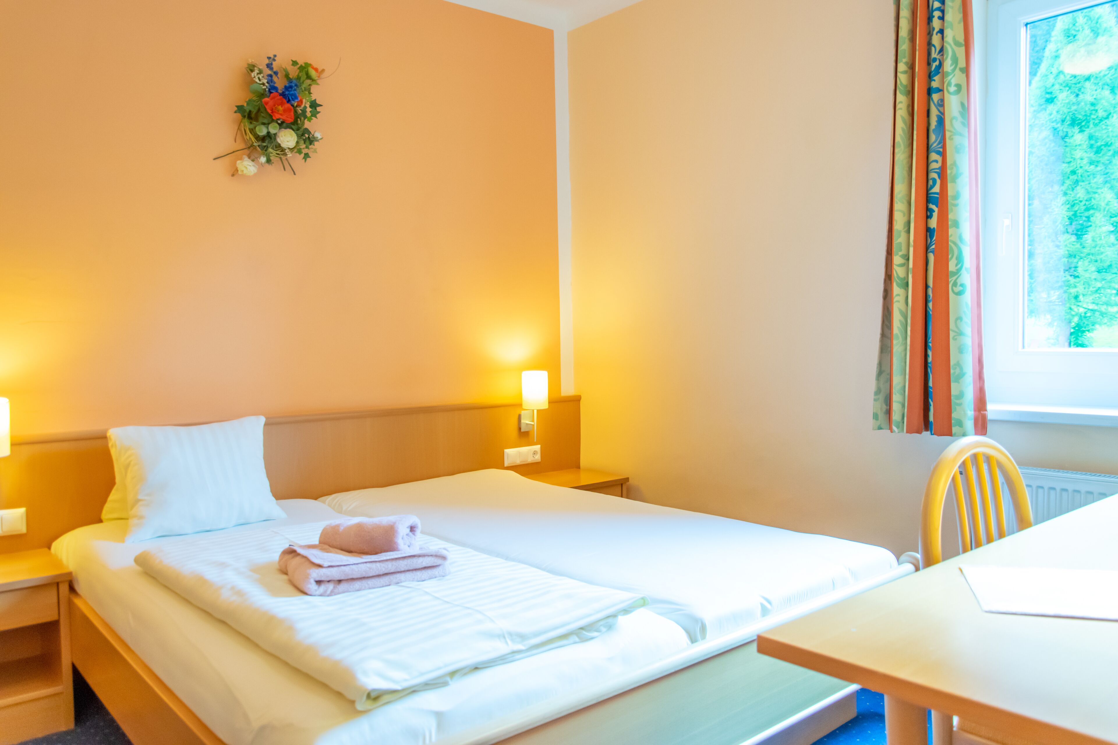 Une chambre d’hôtel avec un lit, des tables de chevet, un bureau et une fenêtre avec des rideaux.
