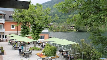 An outdoor café with tables and chairs, surrounded by greenery and overlooking a lake.