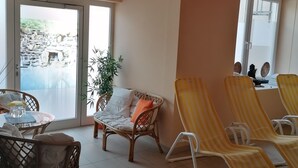 A hotel lobby with a pool view, wicker furniture, and striped lounge chairs. - Strandhotel Burgstaller (Feld am See)