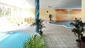 A swimming pool area with lounge chairs, potted plants, and a mural depicting a sunset over water. - Strandhotel Burgstaller (Feld am See)