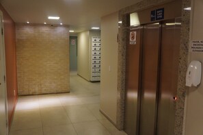 A hotel corridor with an elevator, a no-smoking sign, and a sign indicating a weight limit. - Lindo AP Praia do Forte - Porto Azul 106 (Cabo Frio)