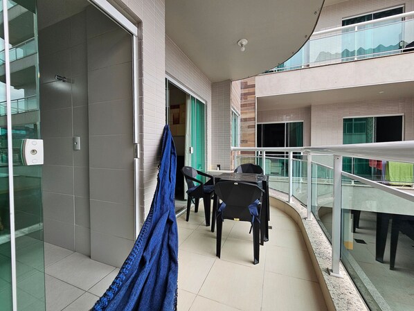 A balcony with a table and chairs, a hanging blue cloth, and a glass railing.