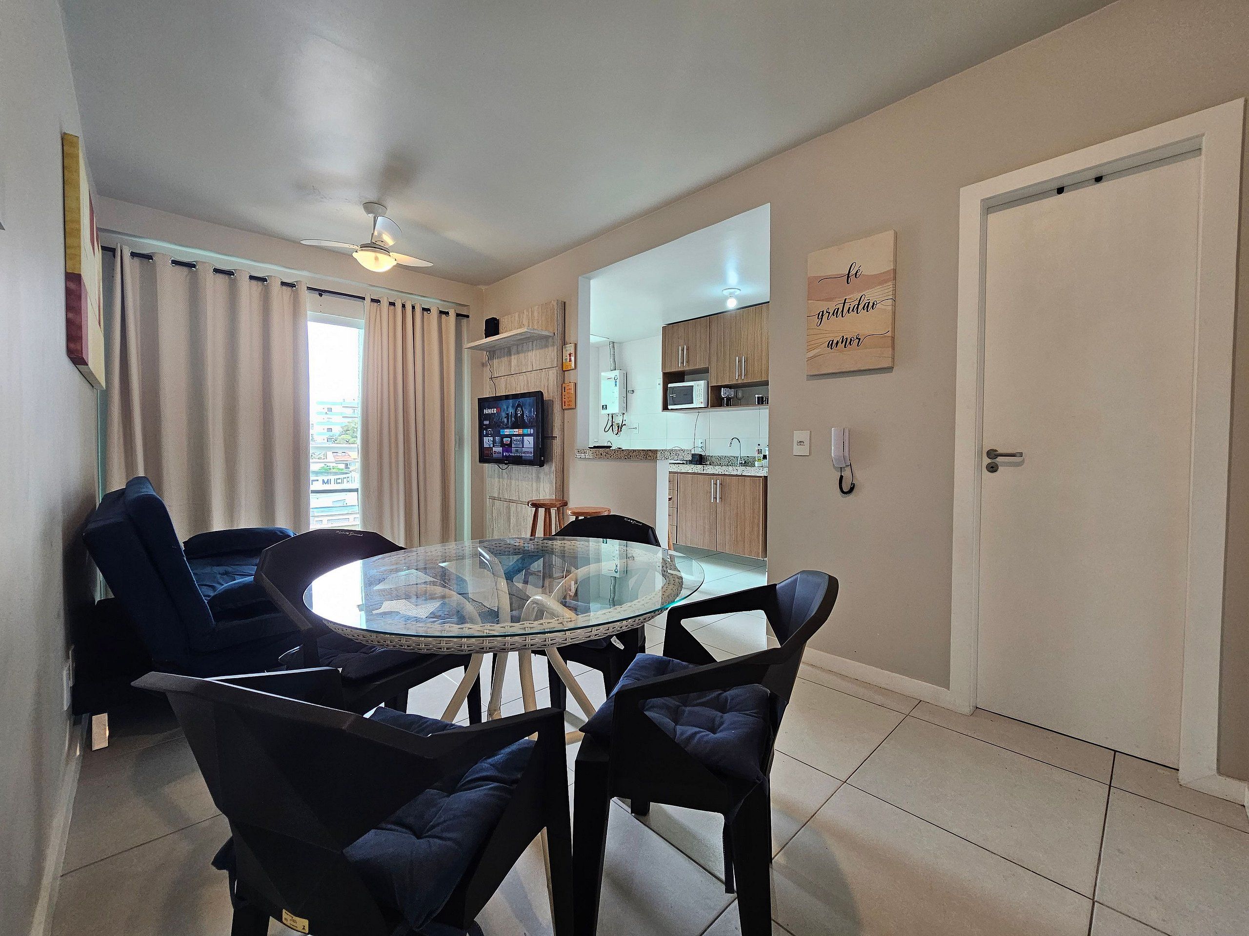 A dining area with a glass table surrounded by chairs, a kitchen in the background, and a door with a sign.