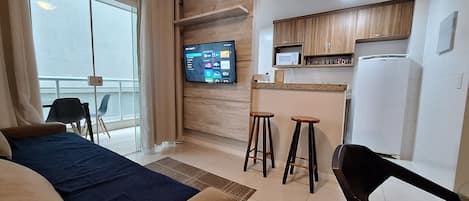 A hotel room with a bed, a TV, a kitchenette, and a balcony.