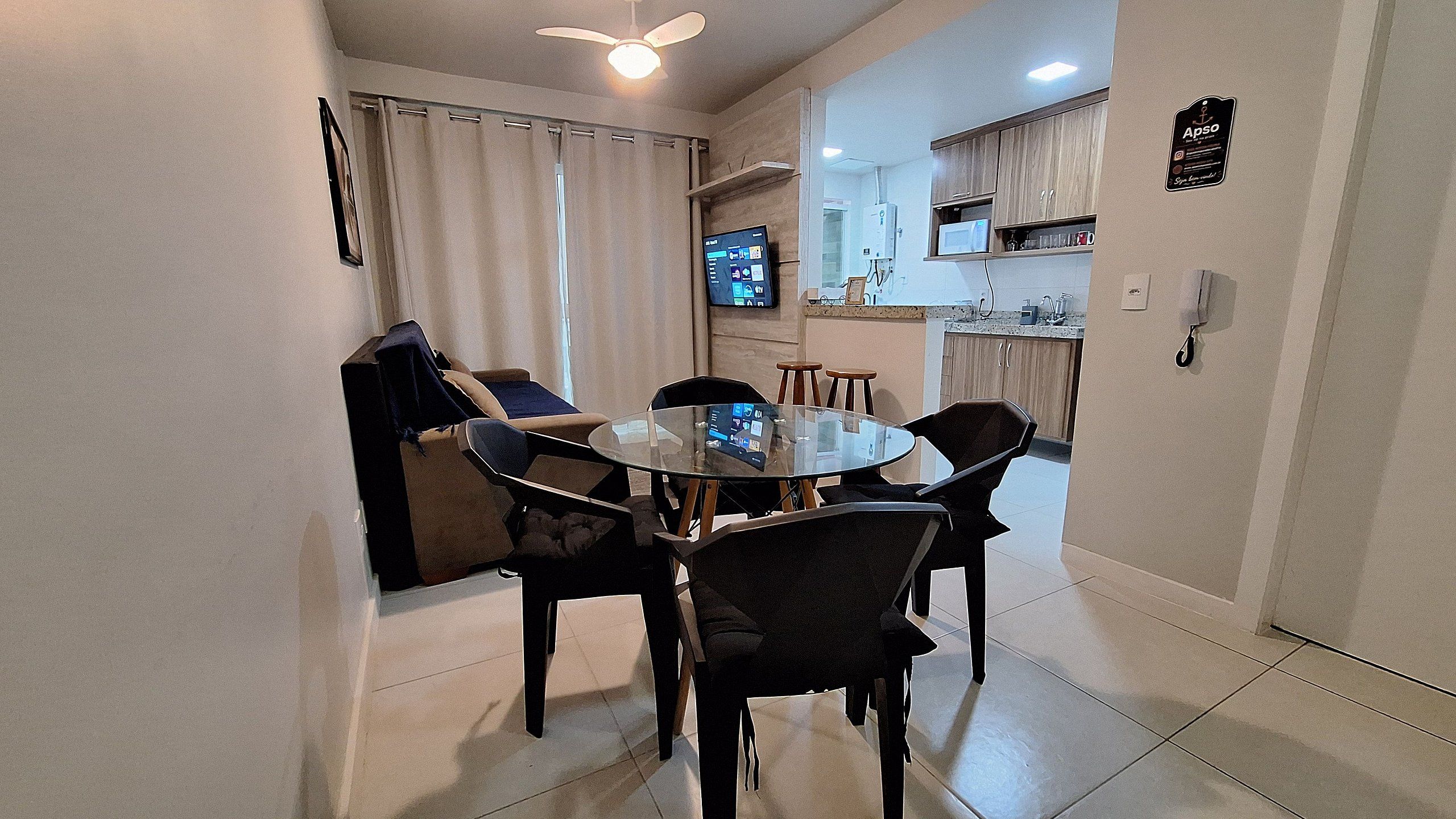 A dining area with a round table and chairs, a ceiling fan, and a kitchen in the background.