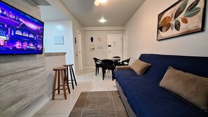 Una sala de estar con televisión, sofá, mesa de centro y un comedor con sillas y mesa.