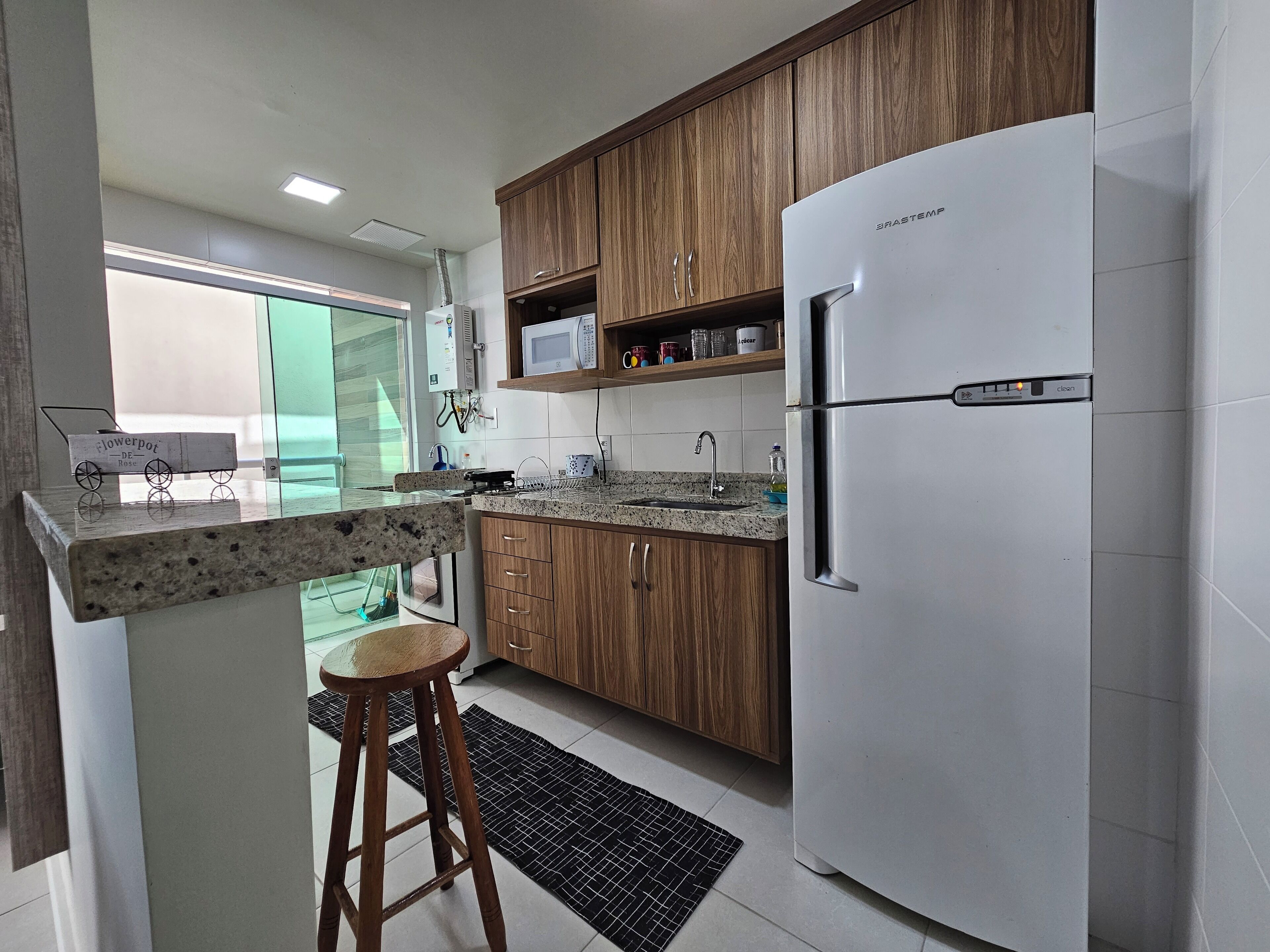 A modern kitchen with wooden cabinets, a stainless steel refrigerator, and a granite countertop.