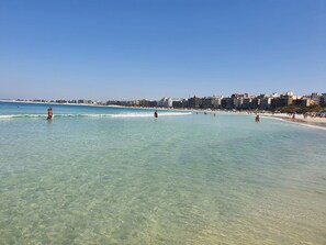 Una playa con aguas cristalinas, gente nadando y edificios al fondo.