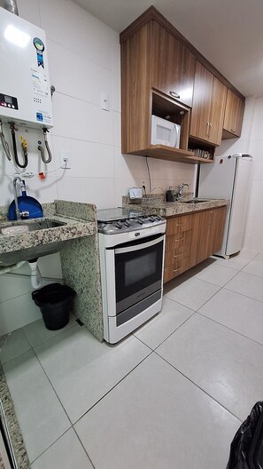 Cocina compacta con estufa a gas, horno y microondas sobre un mueble de madera.