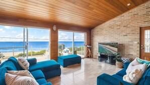 Een ruime woonkamer met een grote televisie, comfortabele zitplaatsen en uitzicht op de oceaan.