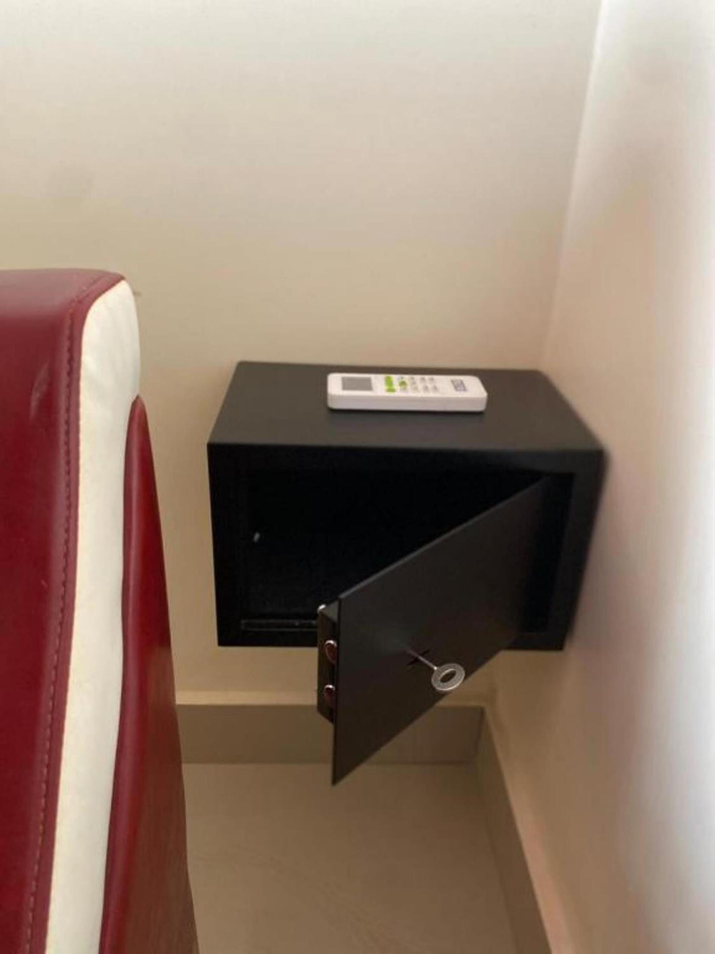 Un comodino nero piccolo con un dispositivo bianco sopra, una sedia rossa e un cassetto socchiuso.