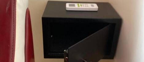 Un comodino nero piccolo con un dispositivo bianco sopra, una sedia rossa e un cassetto socchiuso.