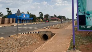 A road with a blue building and a hotel sign advertising a contact number. - YNM Adam's Hotel (Pallisa)