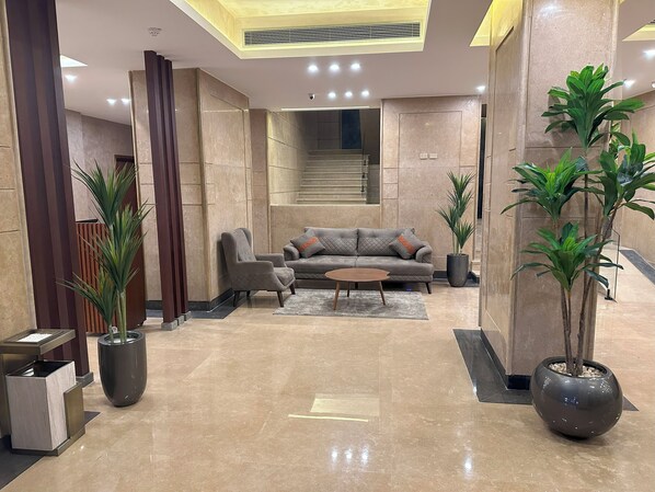 A modern lobby with a grey sofa, a coffee table, and potted plants.