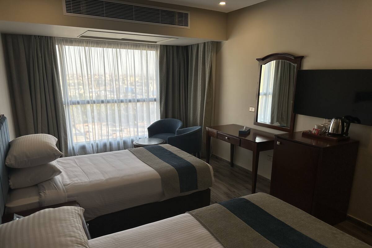 A hotel room with two beds, a desk, a chair, a dresser, a mirror, and a window with curtains.