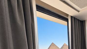 A hotel room with a large window, curtains, a bed, and a view of the pyramids.