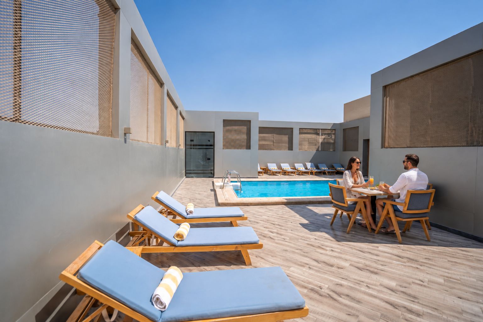 A rooftop pool area with lounge chairs and a dining table.