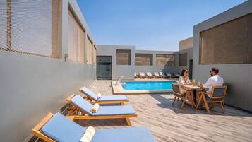 A rooftop pool area with lounge chairs and a dining table.