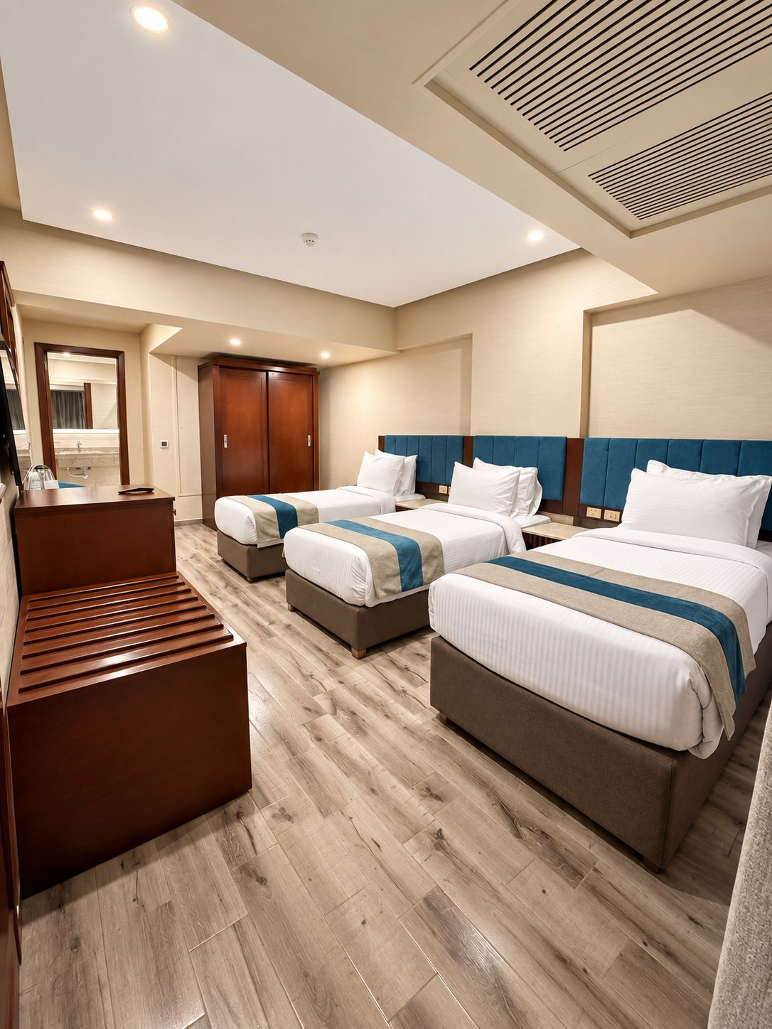 A hotel room with two beds, a wooden bench, a wardrobe, and a mirror.