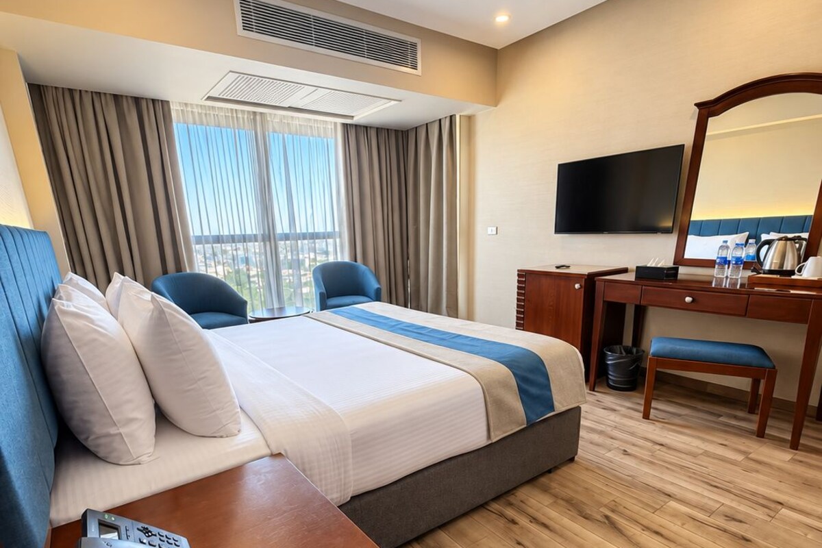 Habitación de hotel con una cama, un escritorio, una silla, un televisor y un teléfono.