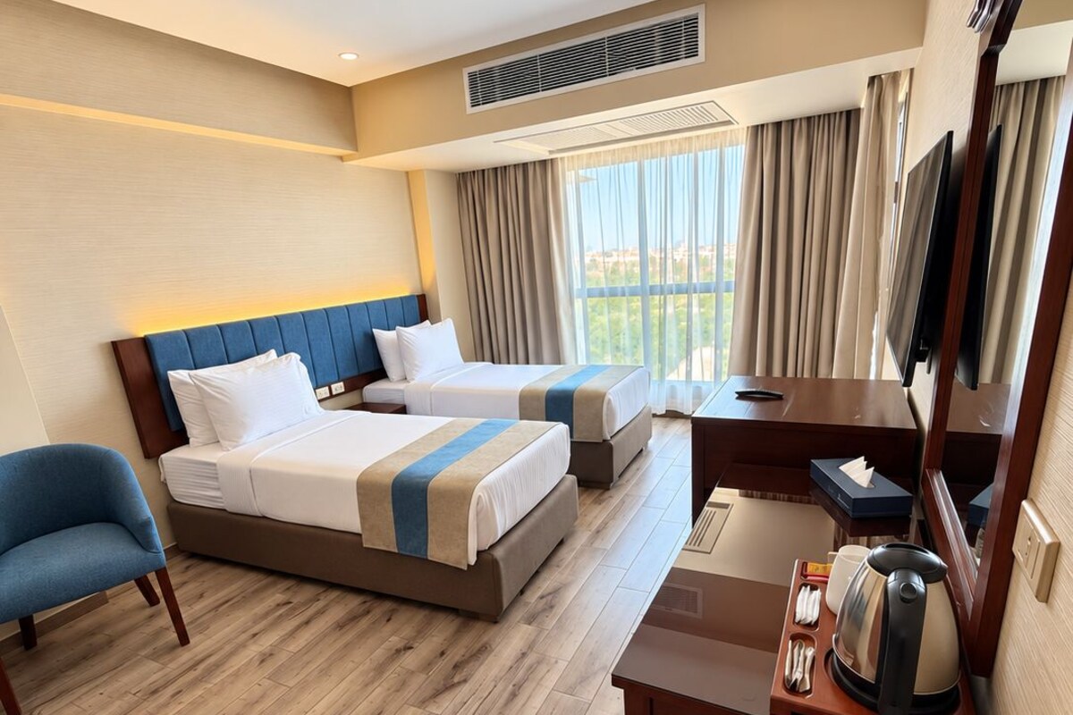 Habitación de hotel con dos camas, un escritorio con hervidor, una silla y un televisor.