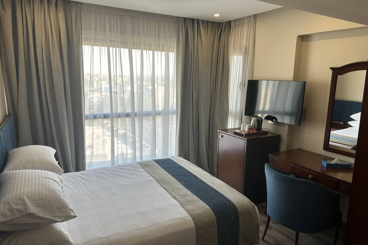 A hotel room with a bed, a desk, a chair, a TV, and a window with curtains.