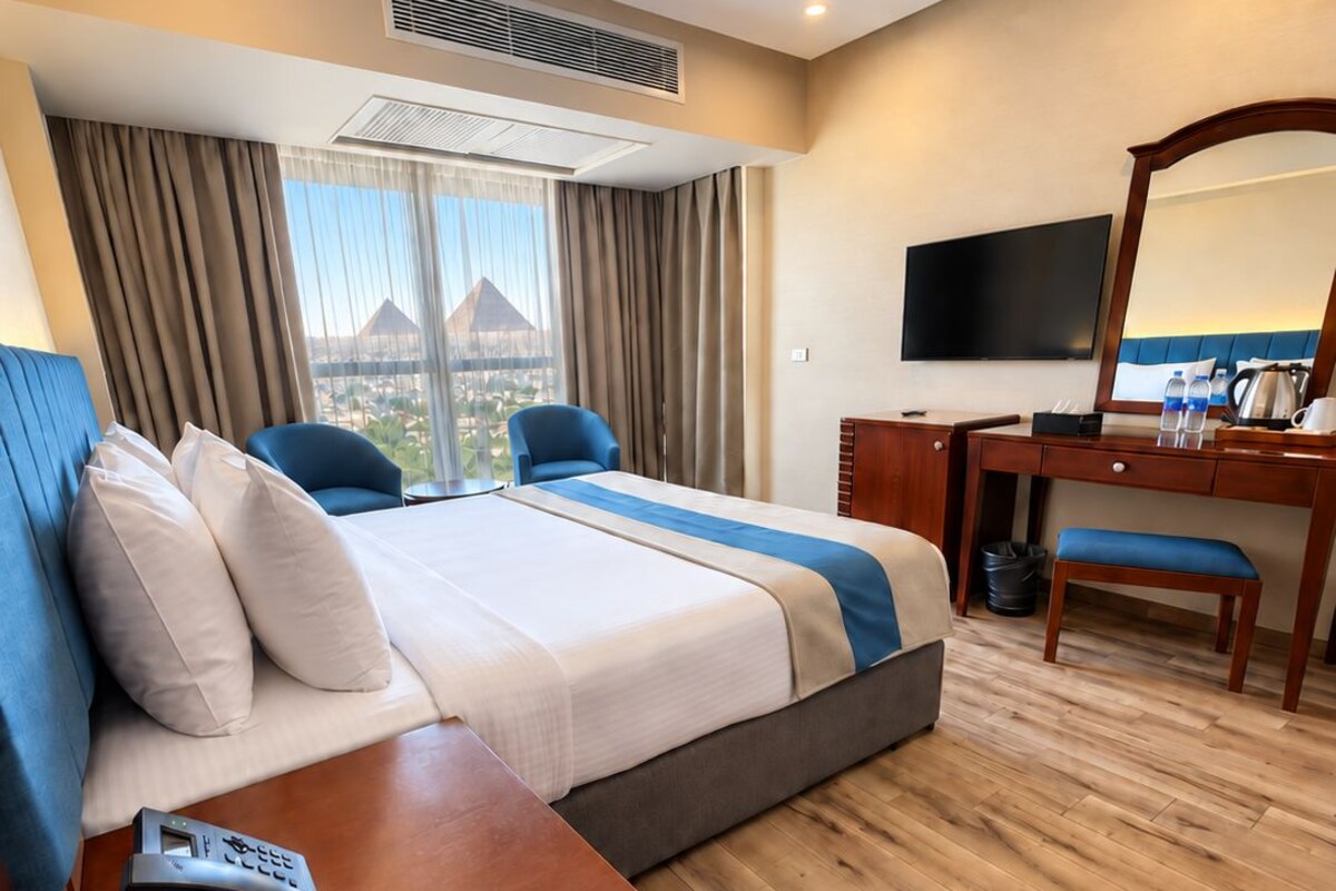 Habitación de hotel con cama, escritorio, silla, televisor y vista a un edificio.