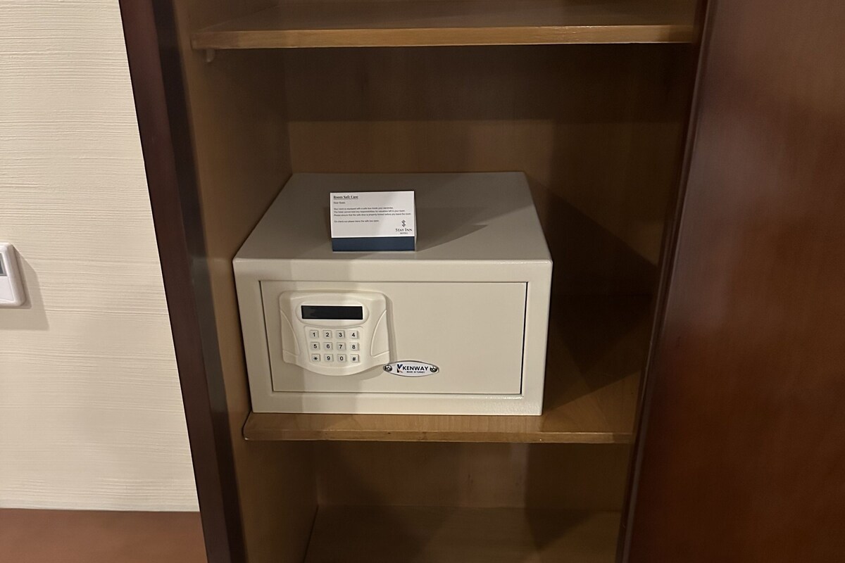 A hotel safe with a keypad and a card reader, a Stay Inn hotel sign, and a pair of slippers on the bottom shelf.