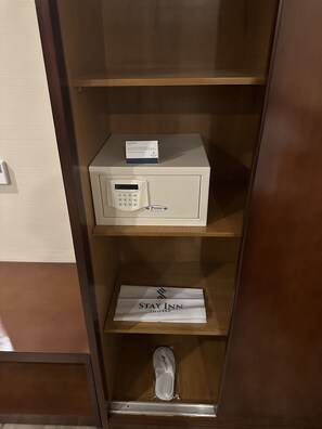 A hotel safe with a keypad and a card reader, a Stay Inn hotel sign, and a pair of slippers on the bottom shelf.