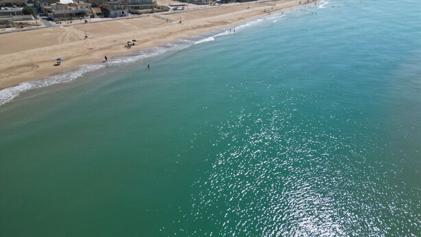 Vista aerea di una zona costiera con spiaggia, edifici e cielo sereno.