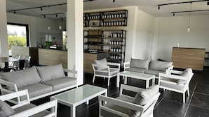 Zona relax moderna con arredi bianchi, una dispensa per vini e una cucina sullo sfondo.