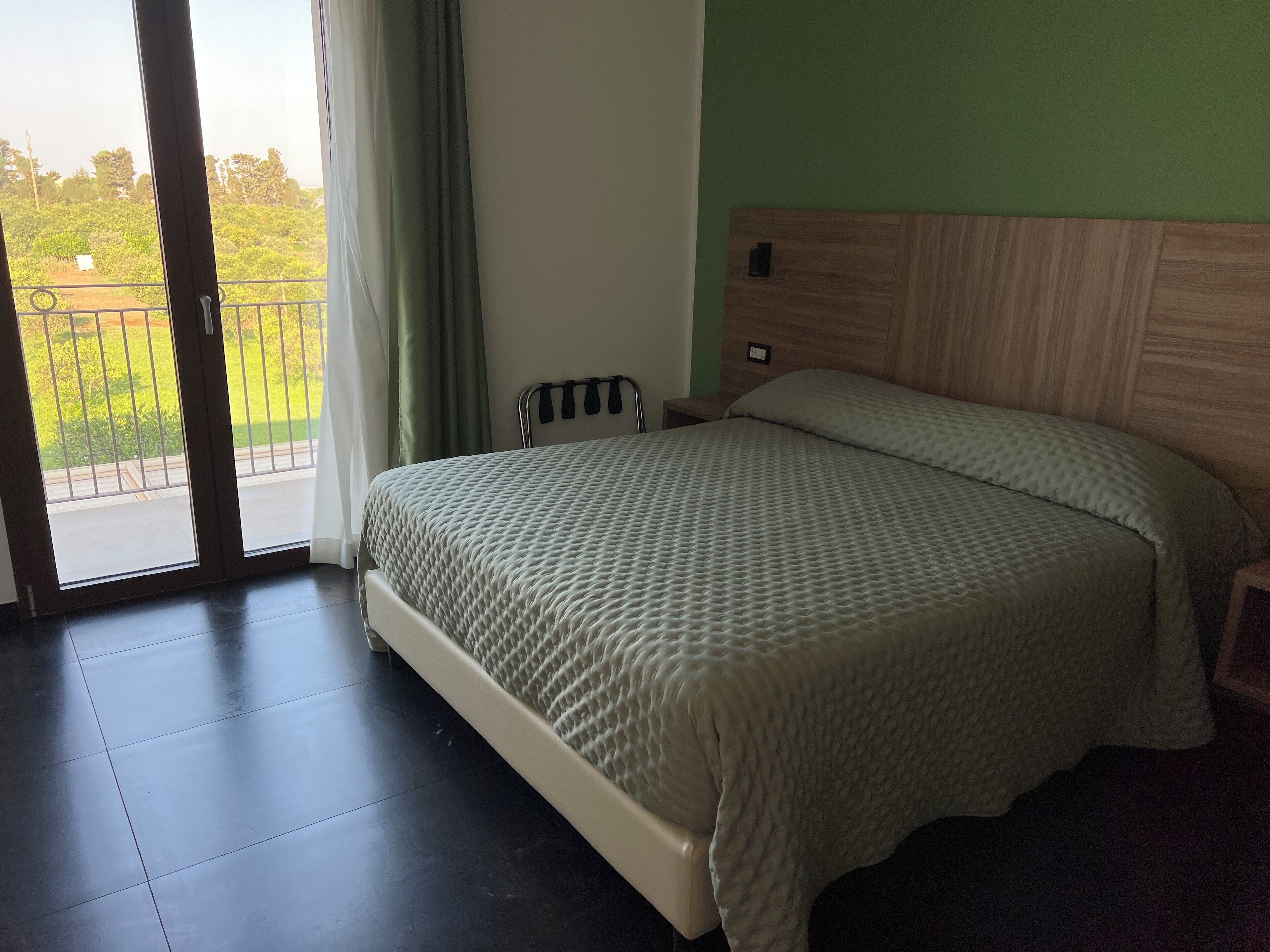 Un dormitorio con cama, mesita de noche, cabecero de madera, ventana con cortinas y vistas al exterior.