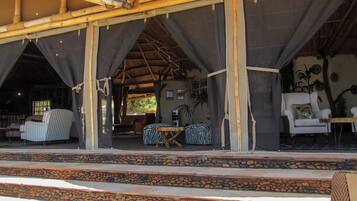 An open-air structure with a thatched roof, stone steps leading up to a seating area with striped and zebra-patterned furniture.
