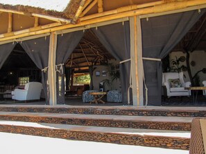 An open-air structure with a thatched roof, stone steps leading up to a seating area with striped and zebra-patterned furniture.