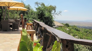 An outdoor seating area with wicker furniture and a wooden deck overlooking a scenic landscape. - Ahadi Mara Camp (Maasai Mara)