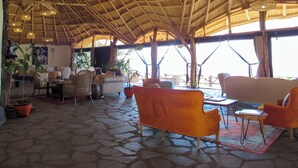 A spacious lounge with a thatched roof, stone flooring, and comfortable seating. - Ahadi Mara Camp (Maasai Mara)