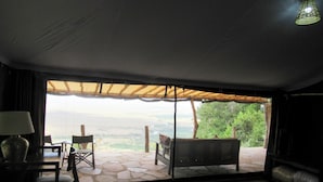 A bedroom with a large bed, a desk, and a chair. There is a view of a patio with a table and chairs. - Ahadi Mara Camp (Maasai Mara)
