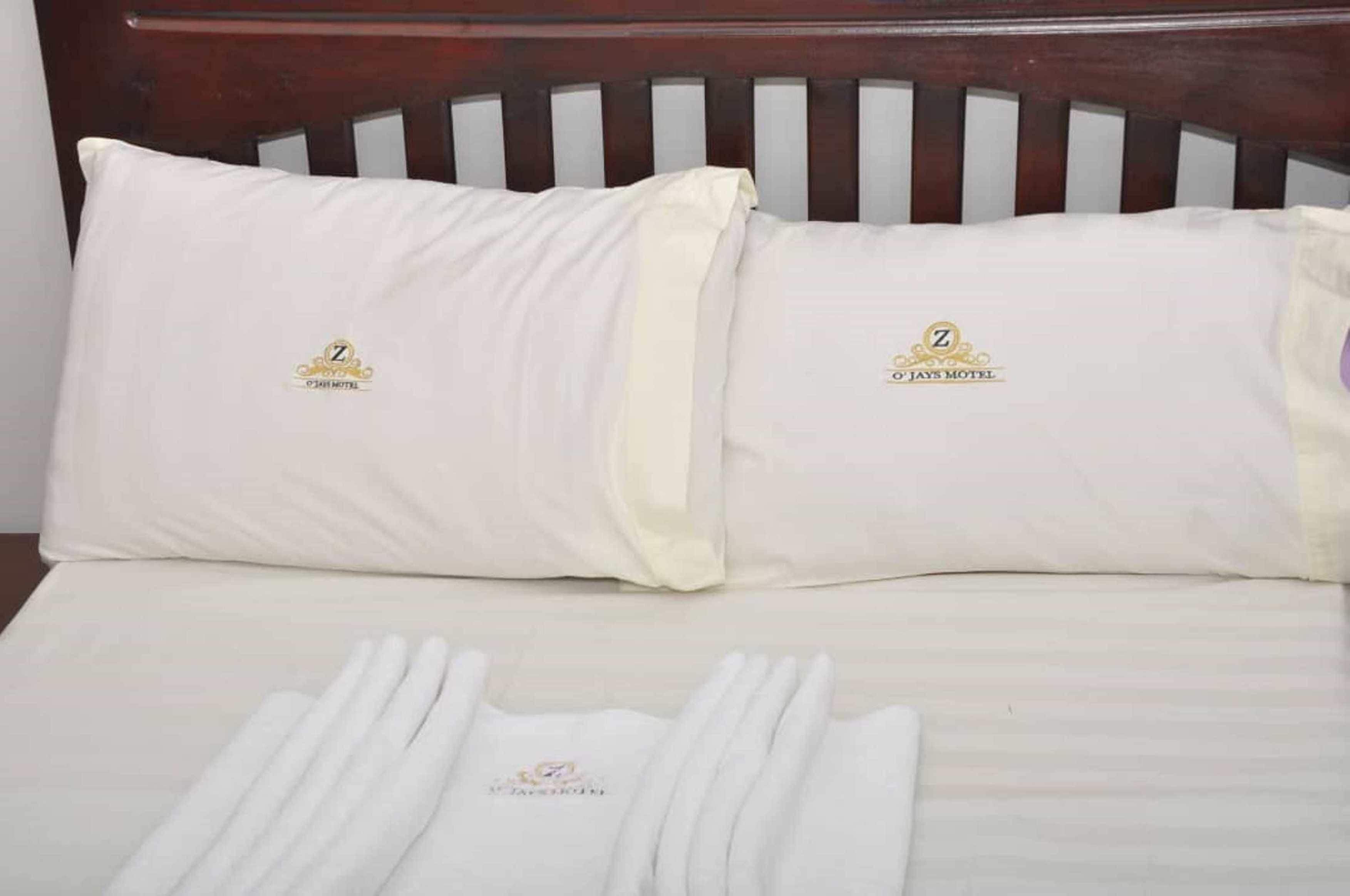 A neatly made bed with white linens and pillows, a wooden headboard, and a towel set on the bed.