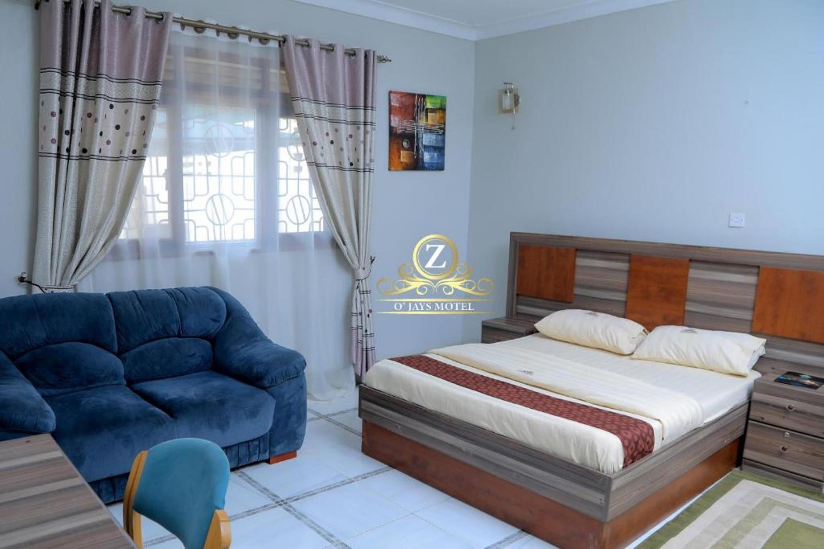 Un dormitorio con una cama, un sofá azul, una mesita de noche de madera y una ventana con cortinas.